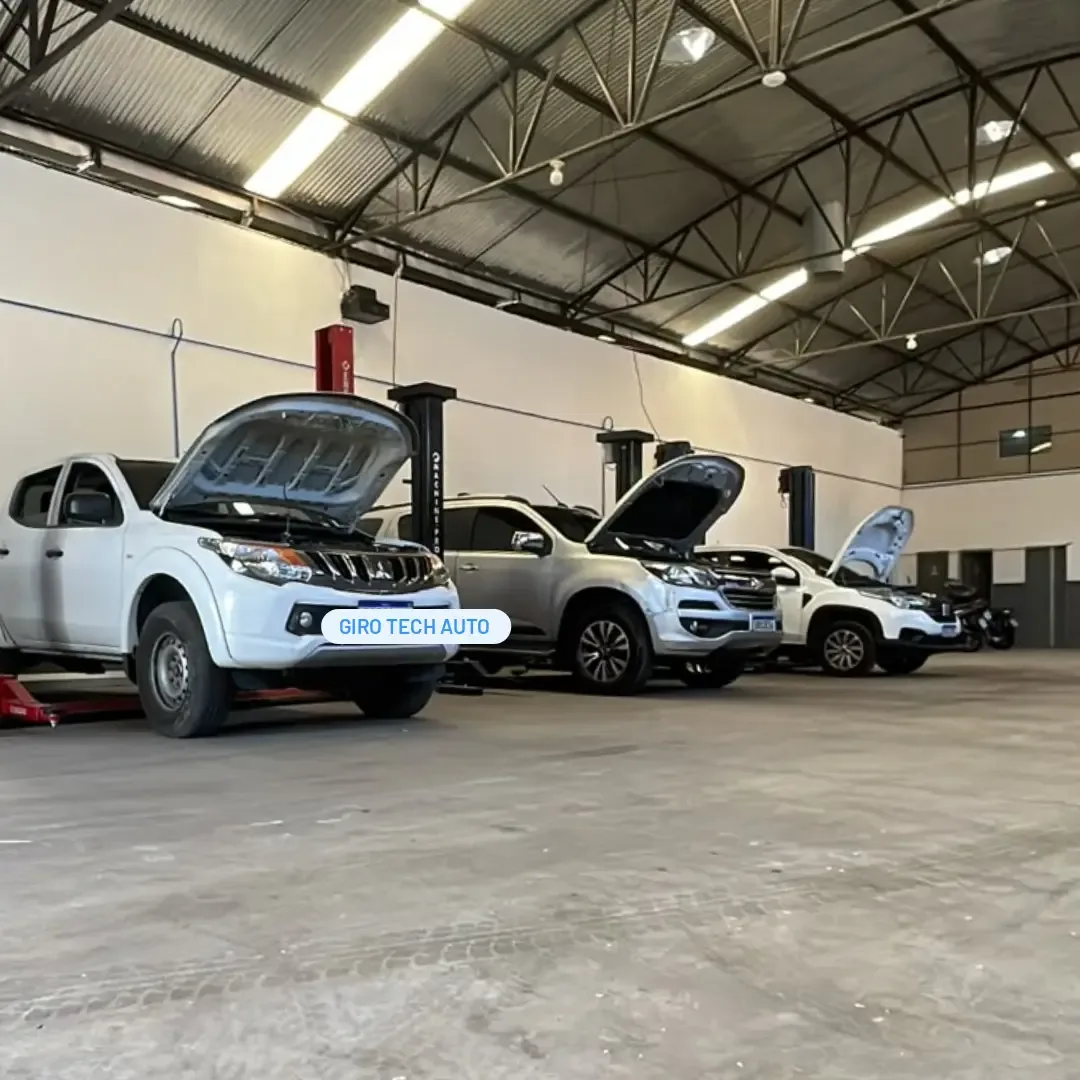 Área de serviço da GiroTech com três picapes em elevadores automotivos, capôs abertos, sob a estrutura metálica do galpão